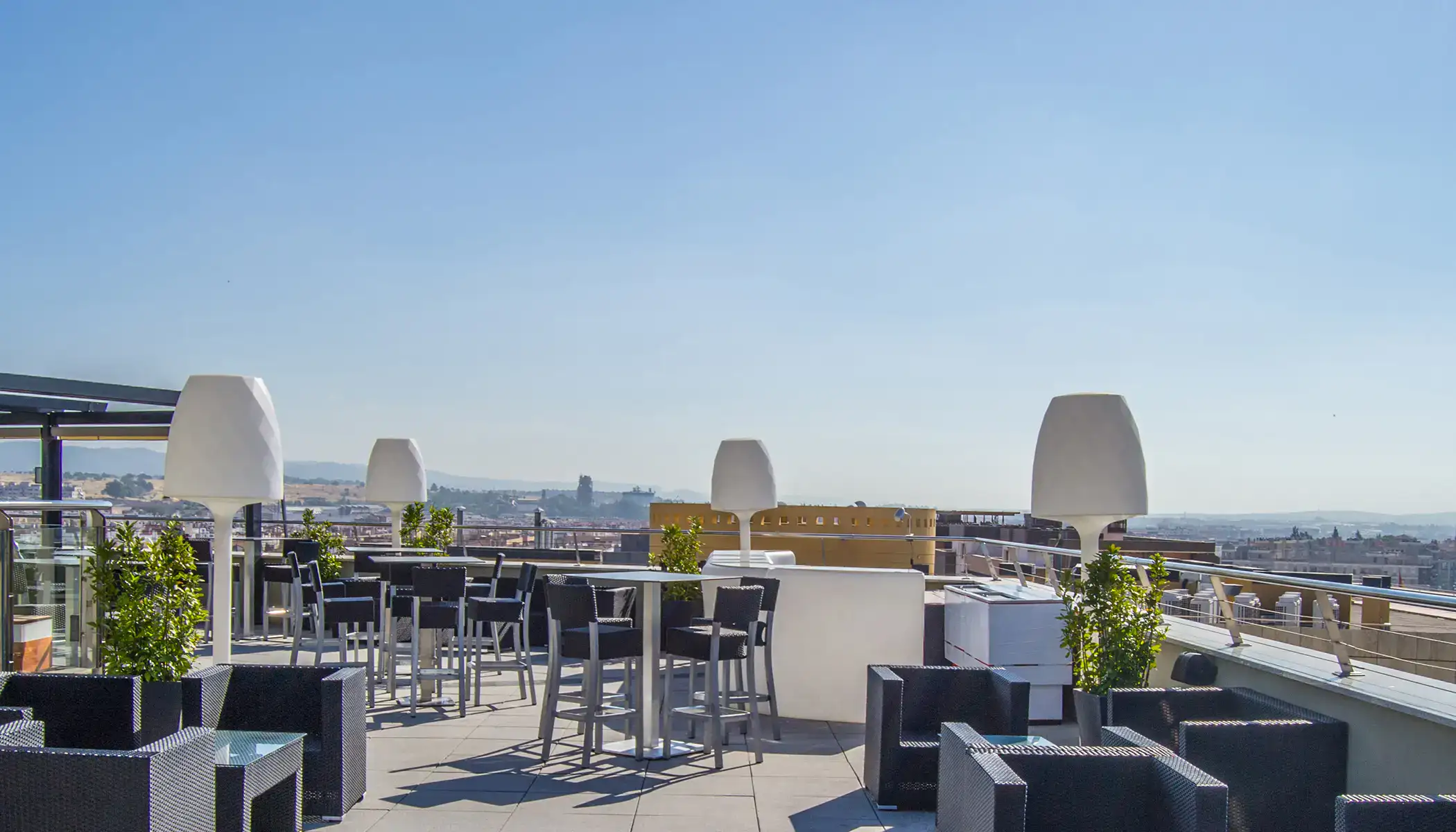 Terraza moderna con mesas y sillas, vista panor&aacute;mica de la ciudad.