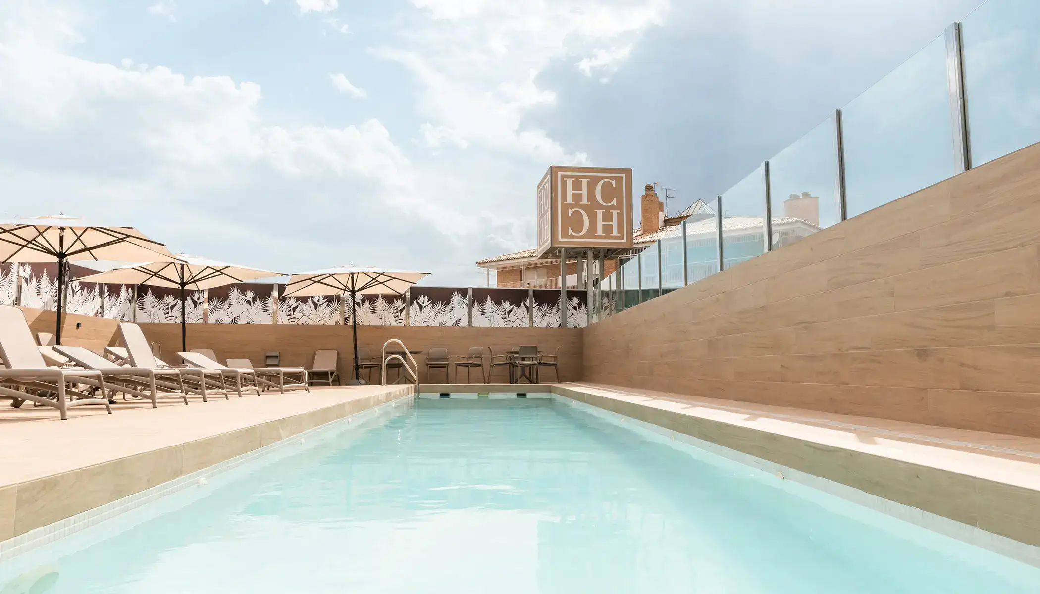 Piscina con tumbonas y sombrillas en un d&iacute;a soleado.