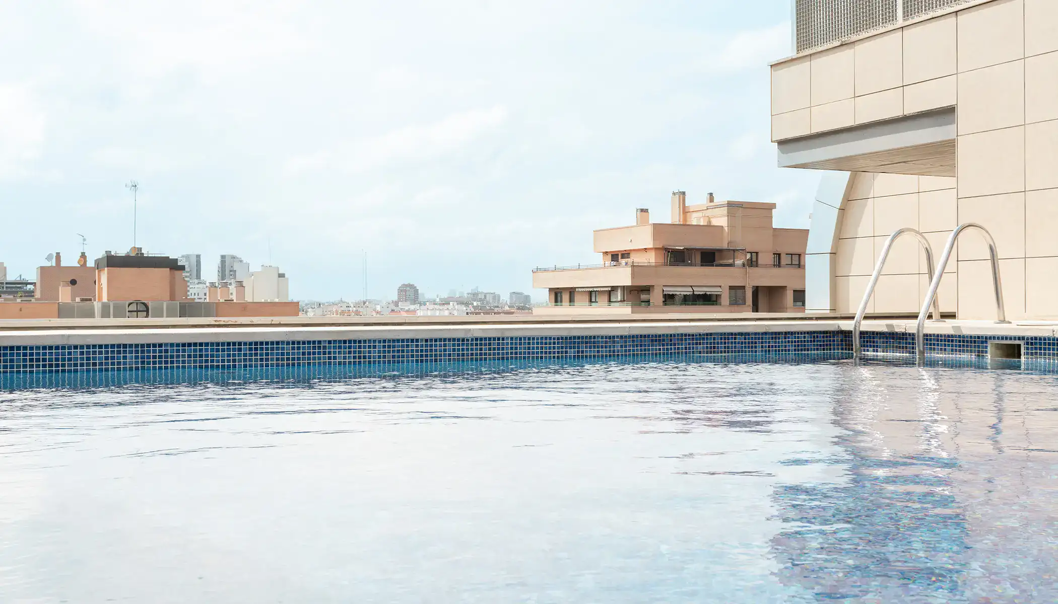 Piscina en la azotea con vista a edificios y cielo nublado.