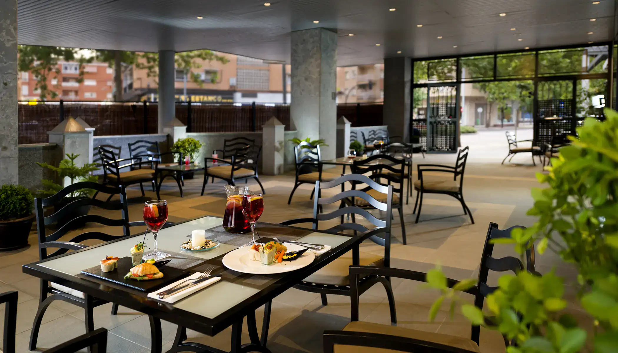 Terraza de restaurante con mesas y sillas, comida servida y copas de vino.