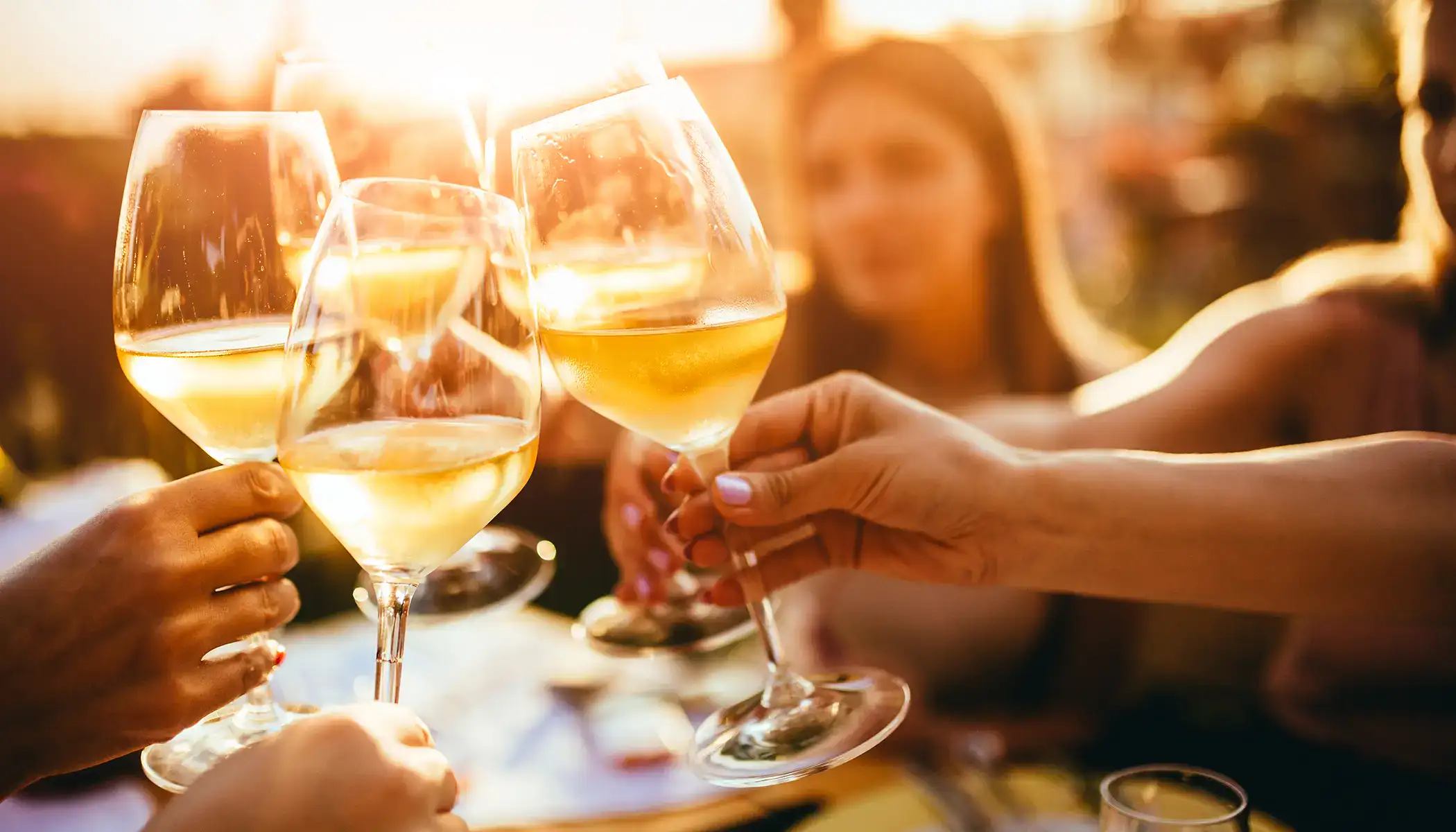 Brindis con copas de vino blanco al atardecer.