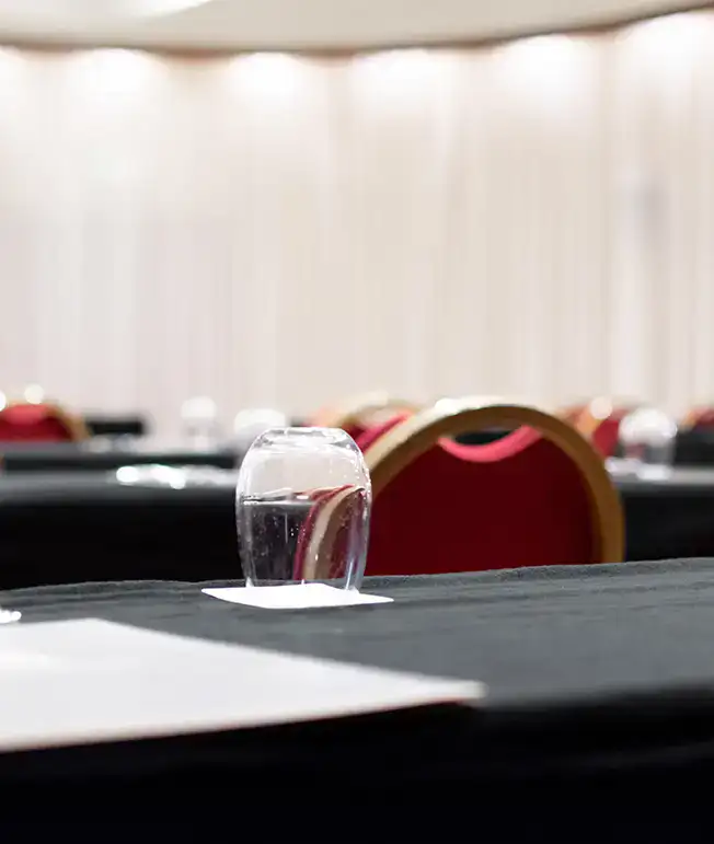 Sala de conferencias vac&iacute;a con sillas rojas y vasos sobre mesas negras.