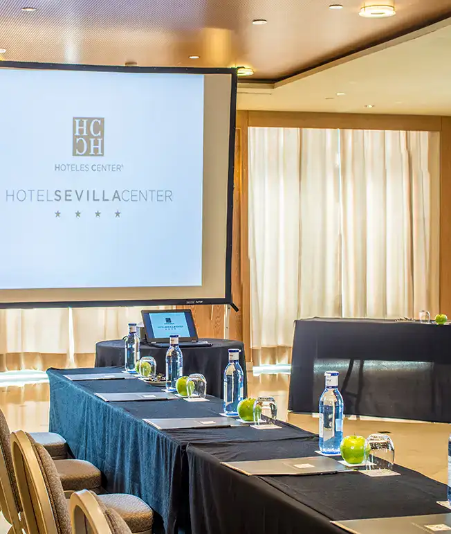 Sala de conferencias con pantalla, mesas, agua y manzanas verdes.