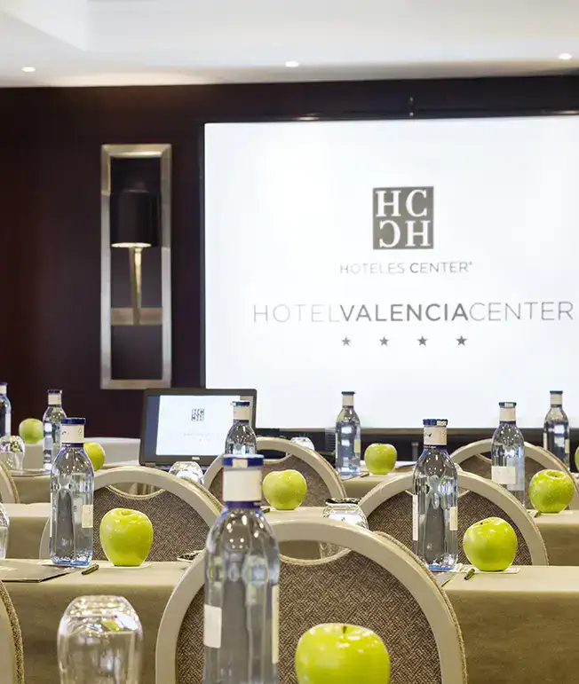 Sala de conferencias con botellas y manzanas sobre las mesas.