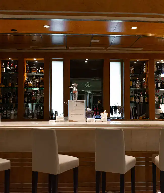 Bar elegante con estantes de licor y sillas blancas frente a la barra.