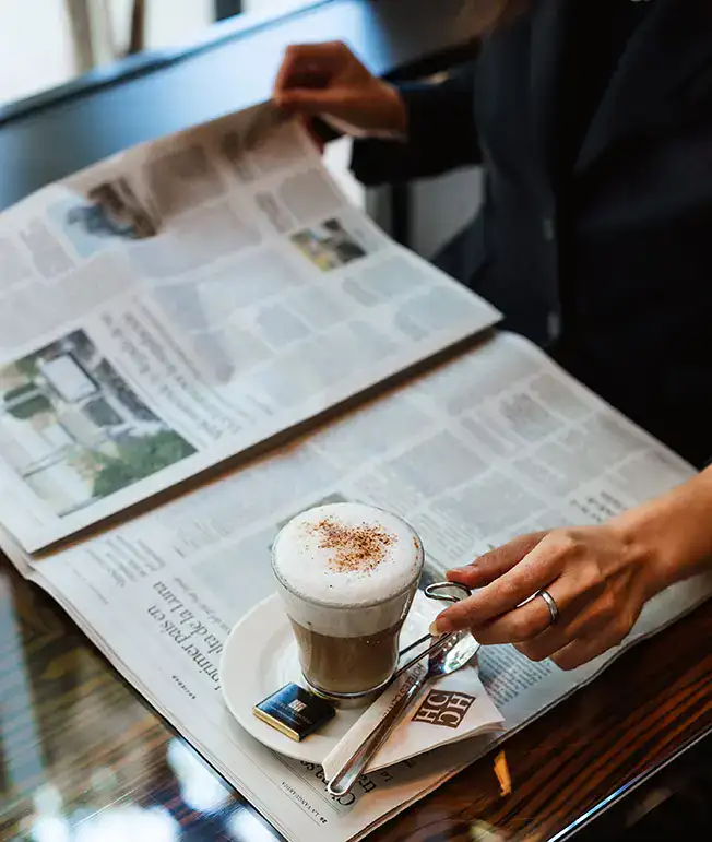 Persona leyendo peri&oacute;dico mientras toma caf&eacute;.