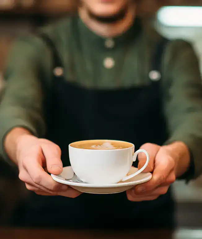 Persona ofreciendo una taza de caf&eacute; con arte latte encima.