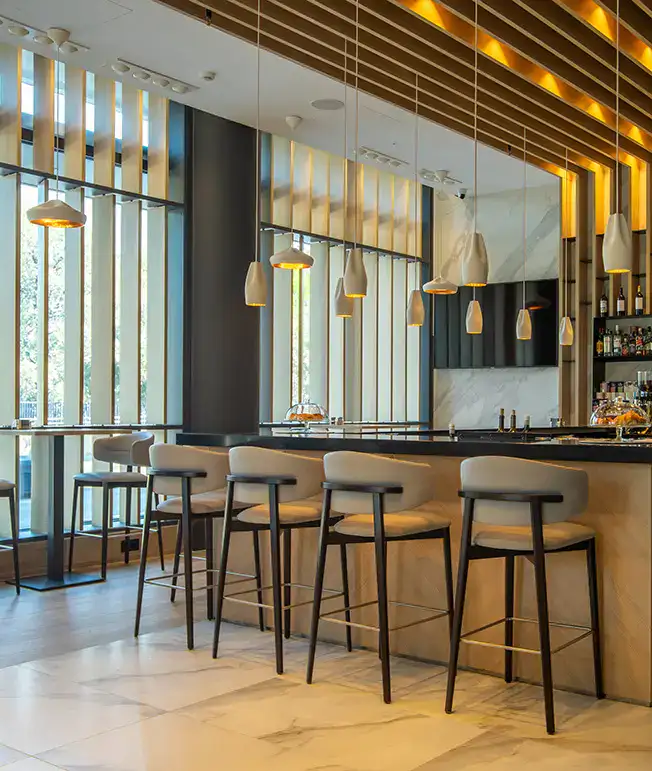 Barra elegante con luces colgantes y taburetes altos en un entorno moderno.