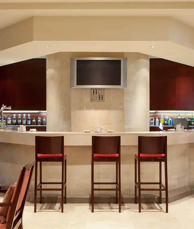 Bar moderno con tres sillas altas y una pantalla apagada en la pared.