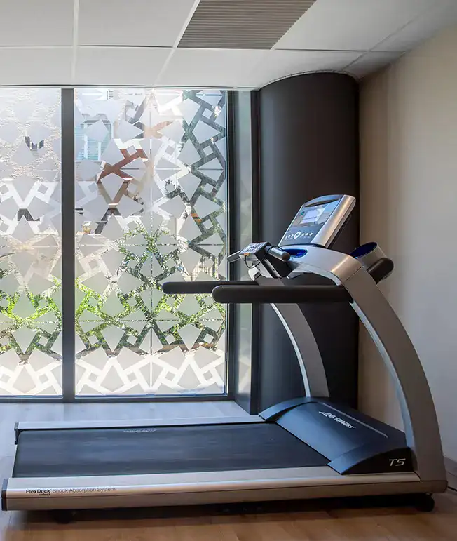 Caminadora frente a una ventana con dise&ntilde;o geom&eacute;trico en el cristal.