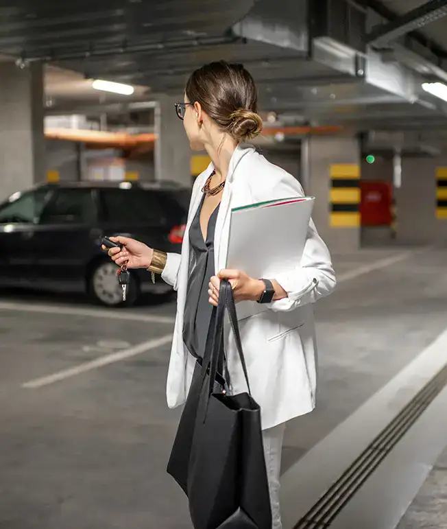 Mujer en estacionamiento, con llaves y documentos, junto a un auto.