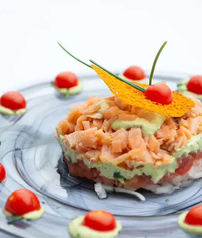 T&aacute;rtaro de salm&oacute;n con adorno de galleta y tomate cherry en plato decorado.
