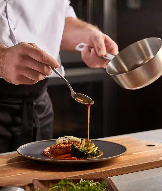 Chef sirviendo salsa sobre un plato gourmet en un restaurante.
