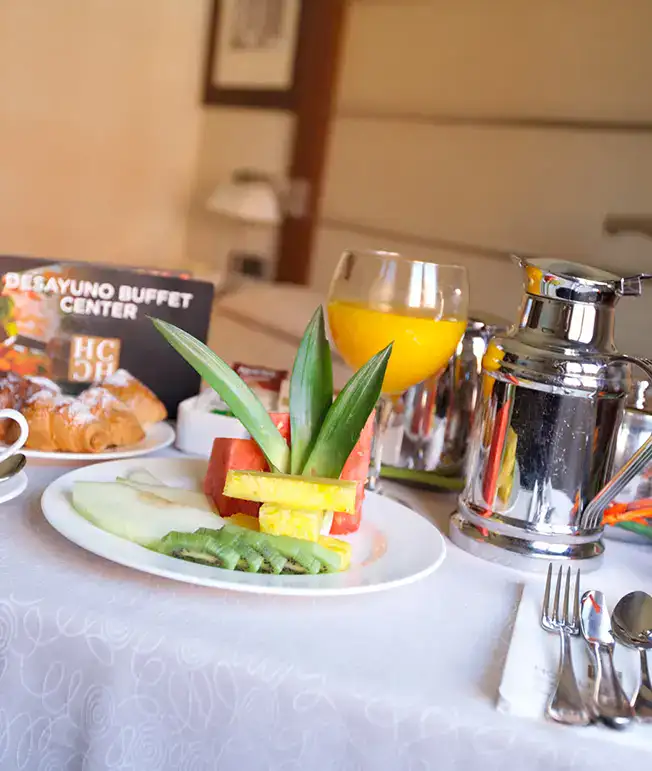 Desayuno con frutas, jugo de naranja y croissants sobre una mesa.
