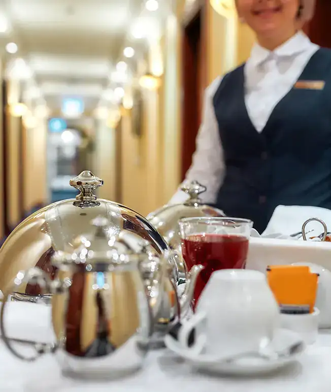 Mesera con bandeja de metal y bebidas en el pasillo de un hotel.