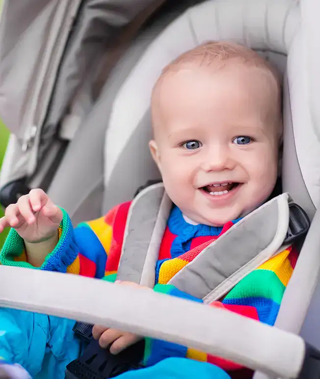 Ni&ntilde;o sonriendo en cochecito, viste su&eacute;ter de colores.