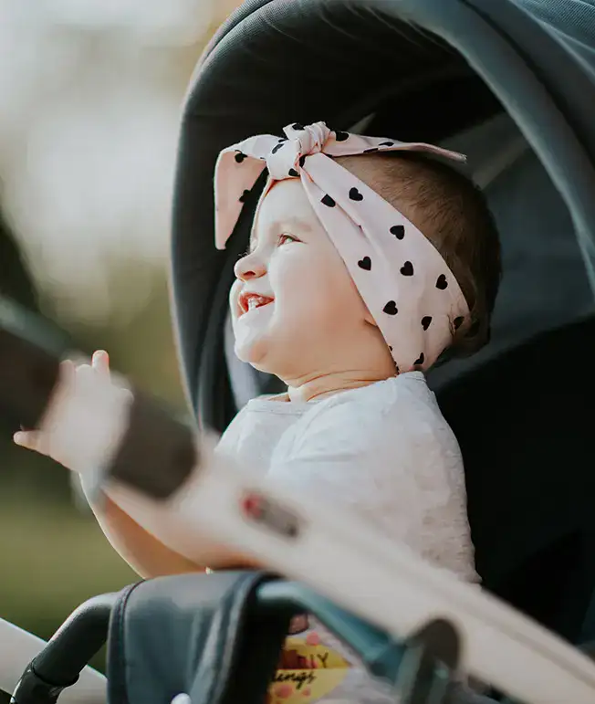 Beb&eacute; sonriente en cochecito con pa&ntilde;uelo de corazones en la cabeza.