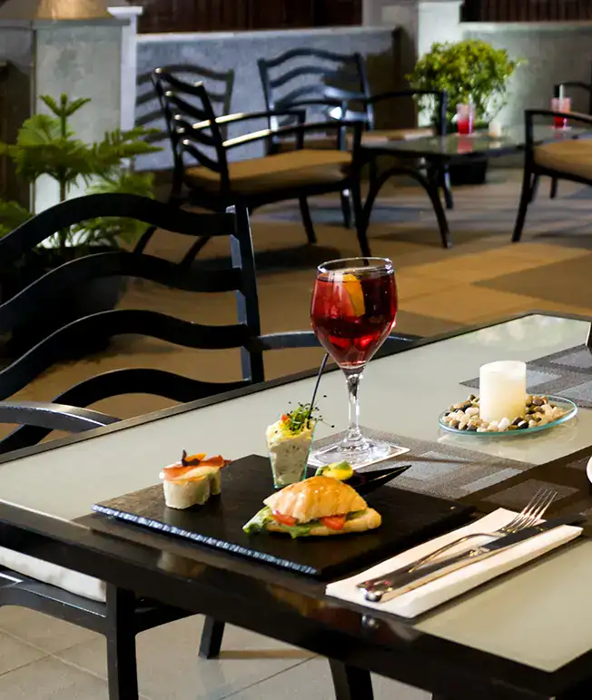 Mesa elegante con aperitivos y una copa de bebida roja al aire libre.