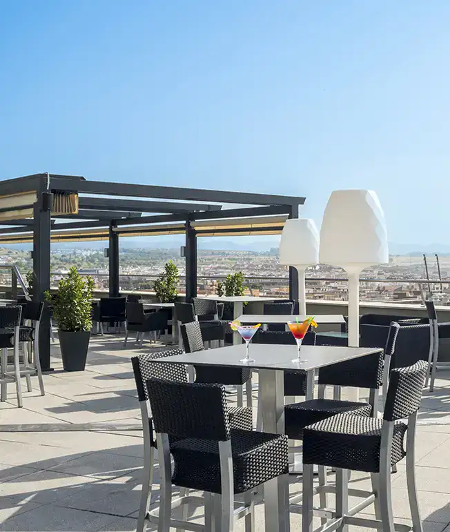 Terraza con muebles de mimbre y copas, vista panor&aacute;mica de la ciudad.
