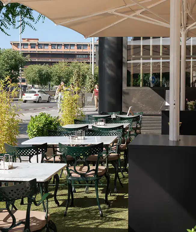 Terraza de cafeter&iacute;a con mesas y sillas vac&iacute;as bajo una sombrilla.