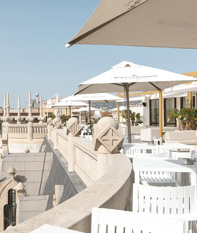Terraza con sombrillas blancas y sillas, con arquitectura ornamental al fondo.