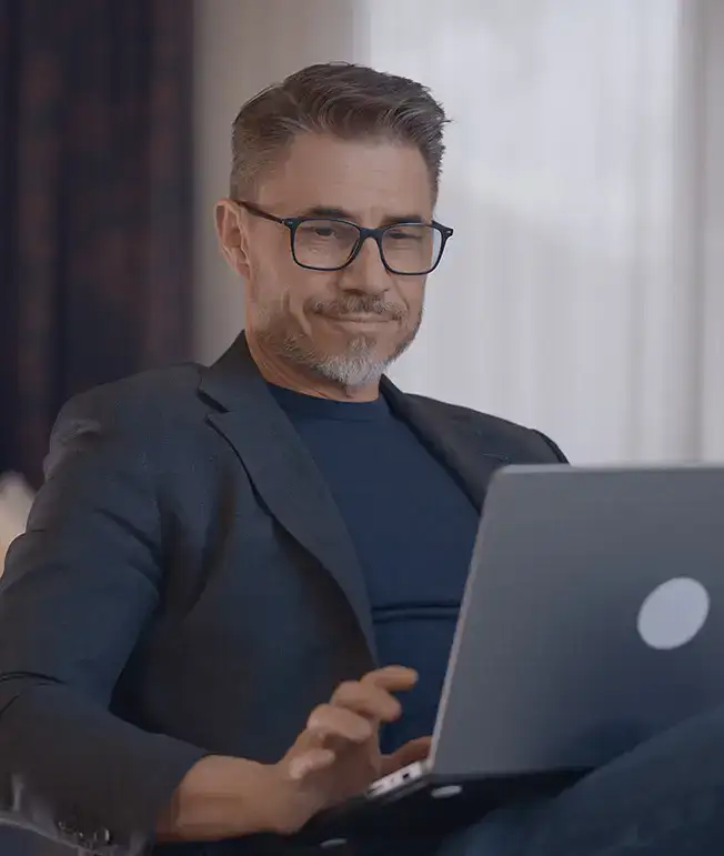 Hombre con gafas usando una laptop en un entorno interior iluminado.