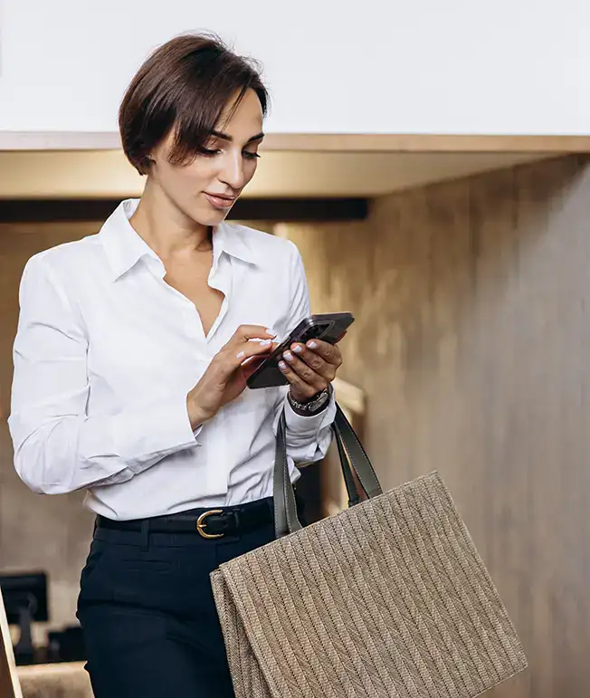 Mujer con bolso revisa su tel&eacute;fono mientras camina por un pasillo.