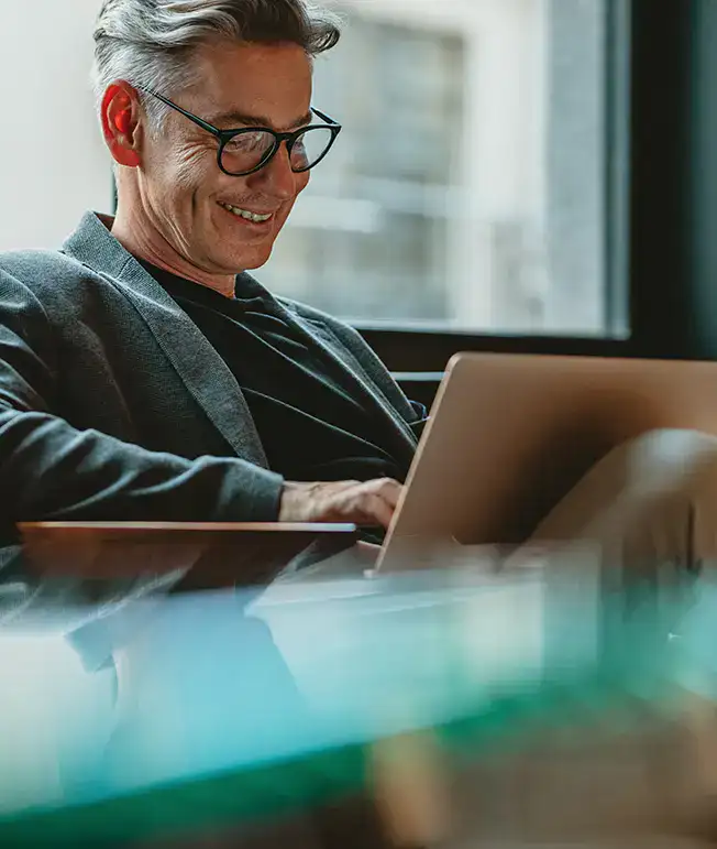 Hombre sonriendo mientras trabaja en una laptop en un espacio luminoso.
