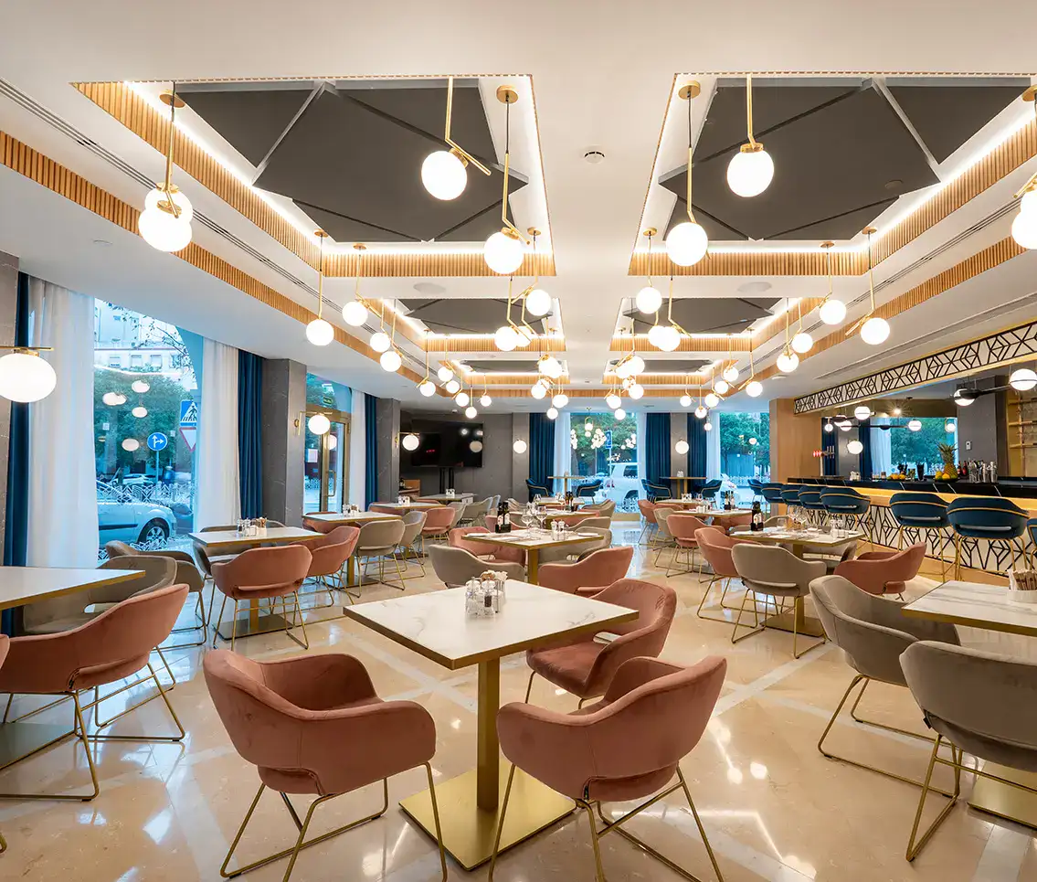 Restaurante moderno con sillas rosadas y luces colgantes circulares.