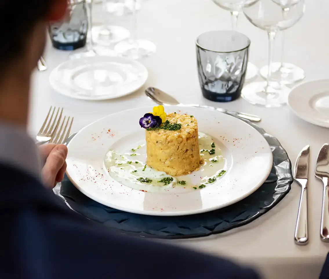 Plato gourmet con decoraci&oacute;n floral en mesa de restaurante elegante.