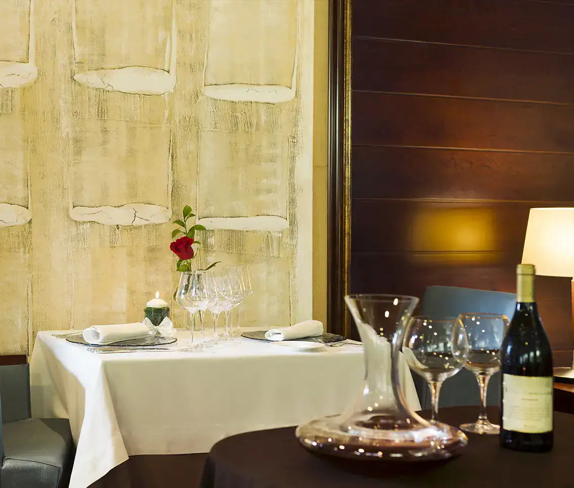 Mesa elegante con vino, copas, rosa roja y vela en restaurante acogedor.