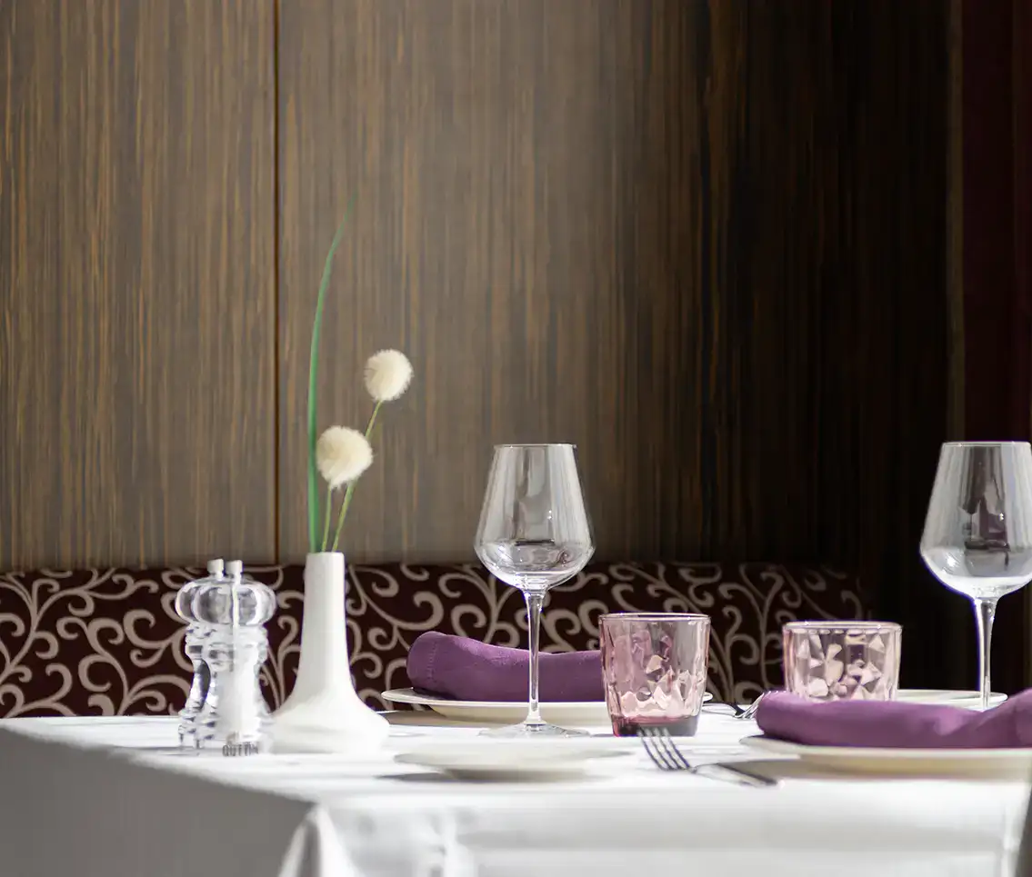 Mesa elegante con copas, vasos rosados y servilletas p&uacute;rpuras en un restaurante.