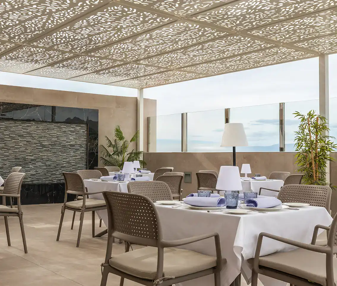 Terraza de restaurante con mesas decoradas y techo con dise&ntilde;o calado.