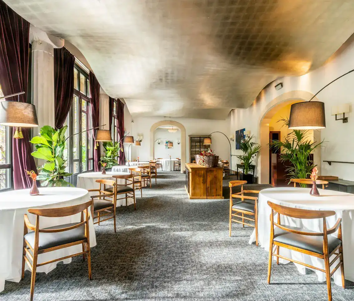 Restaurante elegante con mesas, sillas de madera y plantas decorativas.