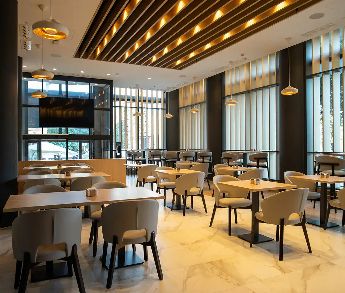 Restaurante moderno con mesas y sillas vac&iacute;as, luz c&aacute;lida y decoraci&oacute;n elegante.