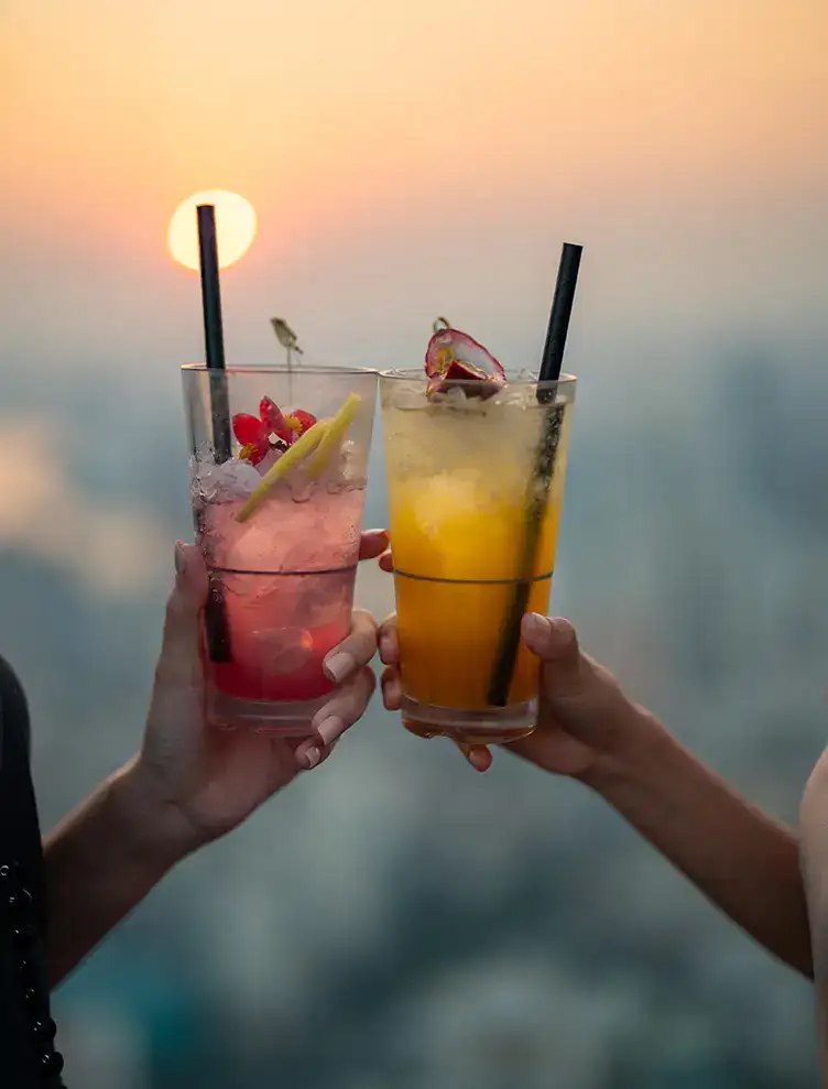 Dos manos brindan con c&oacute;cteles al atardecer.