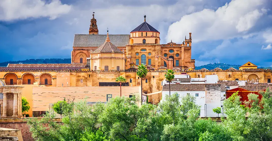 Edificio hist&oacute;rico rodeado de vegetaci&oacute;n bajo un cielo nublado.