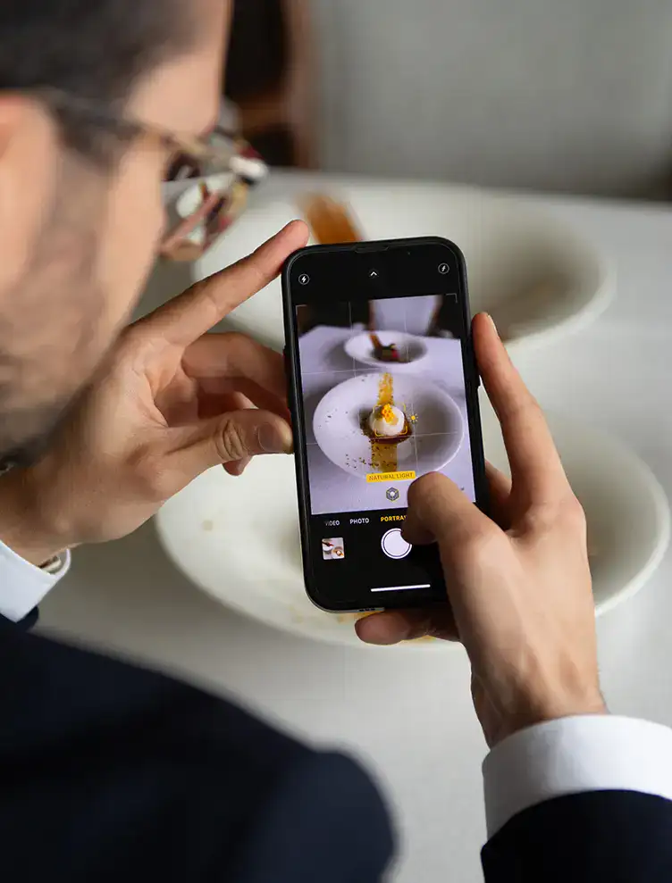 Hombre tomando foto de plato con su smartphone en una mesa.
