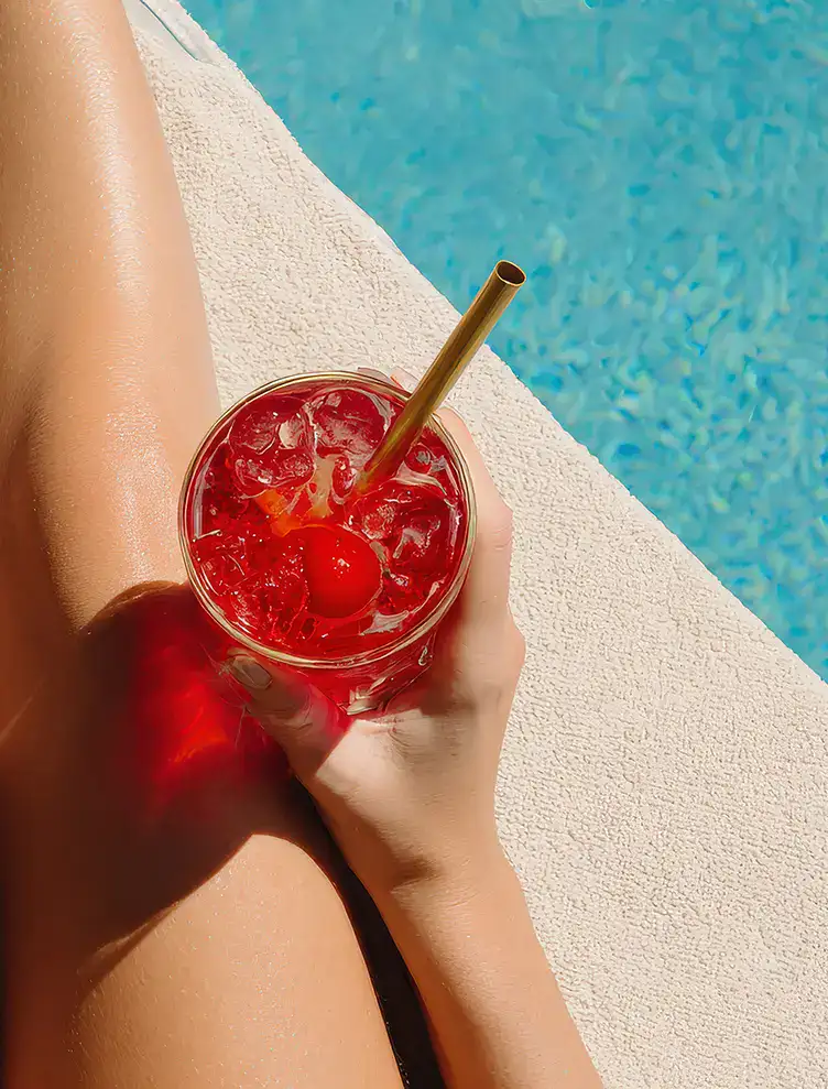 Persona sosteniendo una bebida roja junto a una piscina.