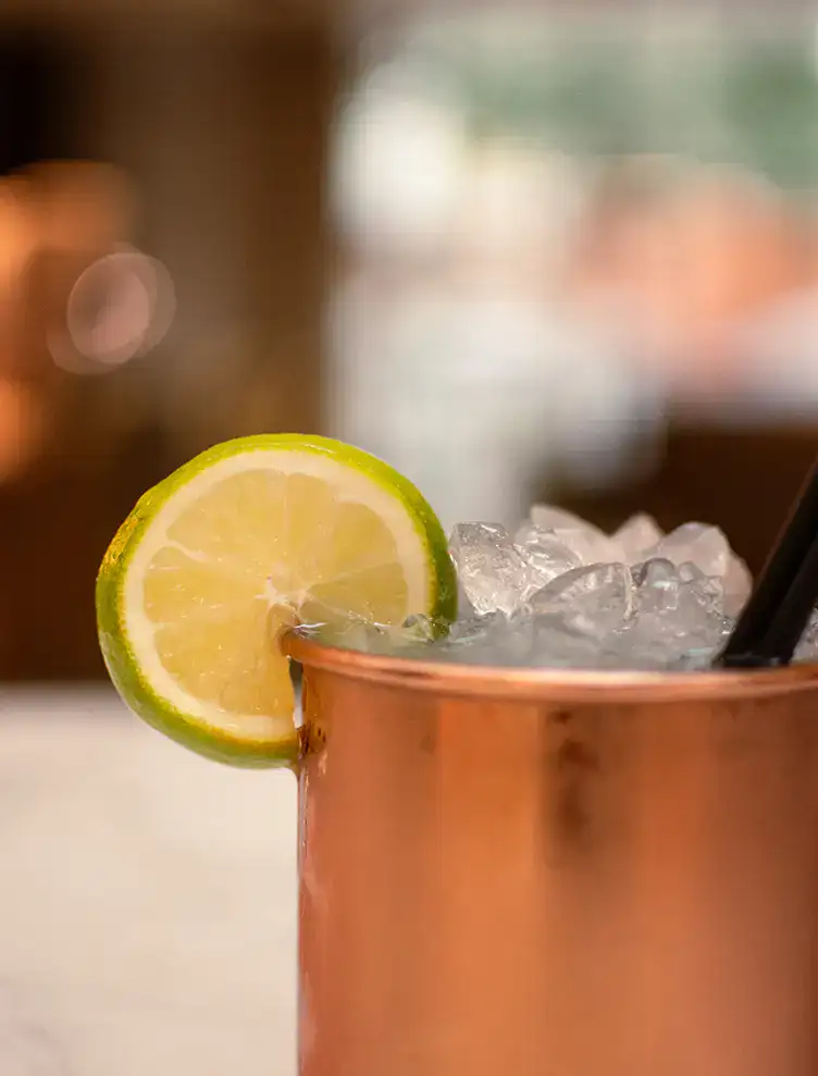 Vaso de cobre con hielo, rodaja de lim&oacute;n y popote negro.