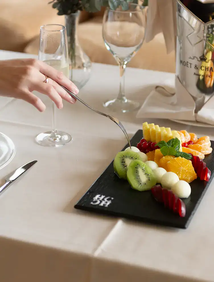 Plato de frutas frescas en mesa elegante con copas y cubiertos.