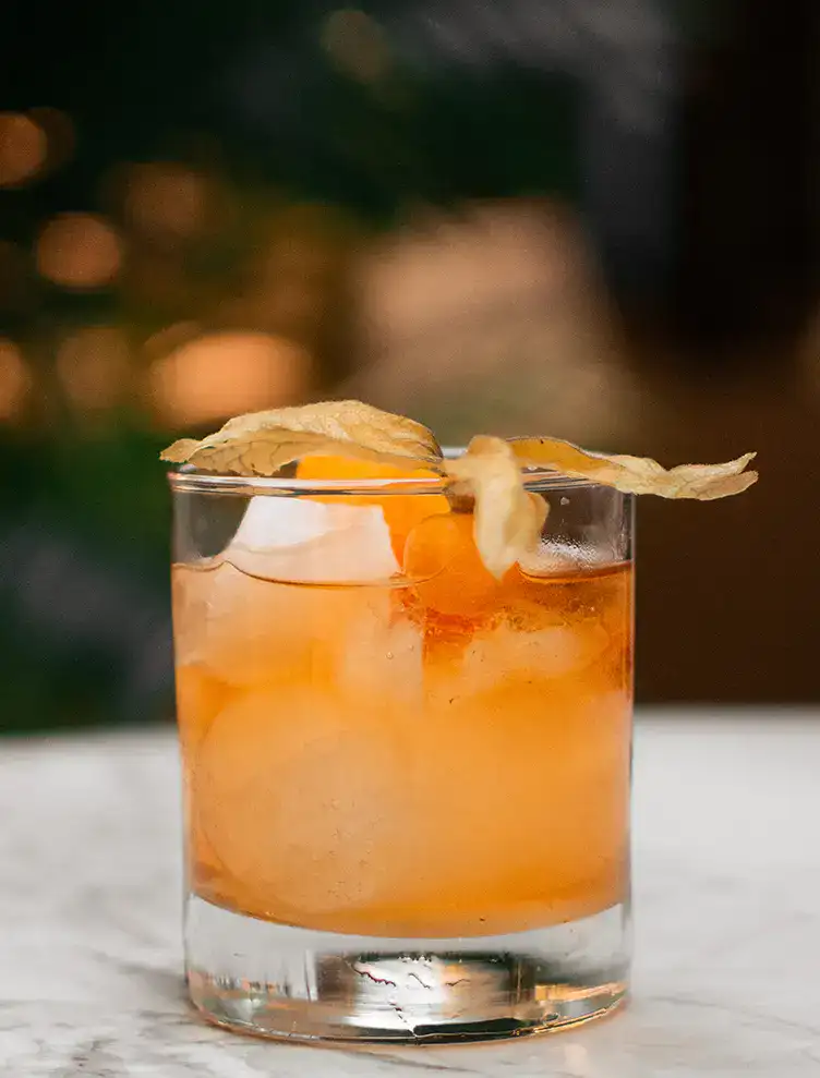 C&oacute;ctel naranja con hielo y decoraci&oacute;n en vaso sobre mesa blanca.