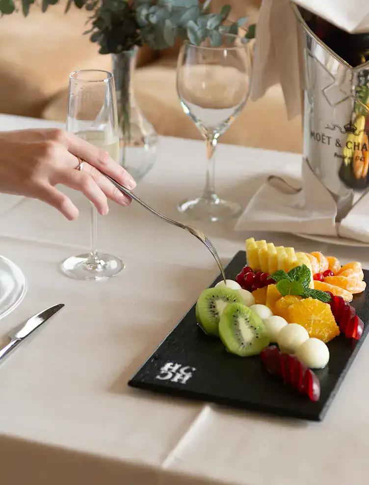 Mujer con tenedor tomando fruta de una bandeja en una mesa elegante.