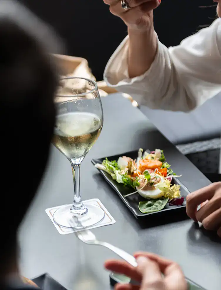 Persona disfrutando una ensalada con vino en un restaurante elegante.