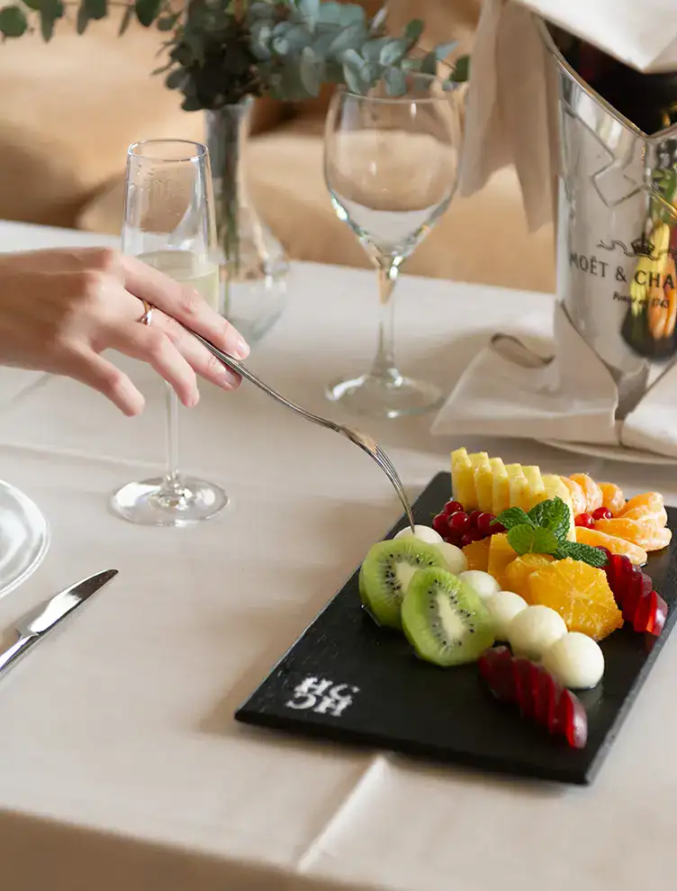 Plato de frutas frescas en mesa elegante con copa de champ&aacute;n.
