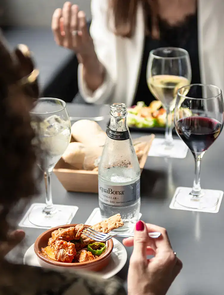 Dos personas cenan con vino, agua y tapas en una mesa.