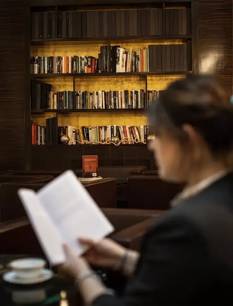 Persona leyendo en una biblioteca acogedora con estantes llenos de libros.