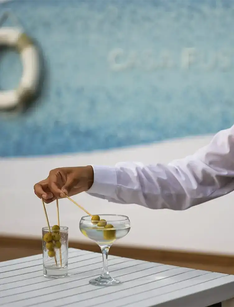 Persona colocando aceitunas en dos copas sobre mesa blanca.