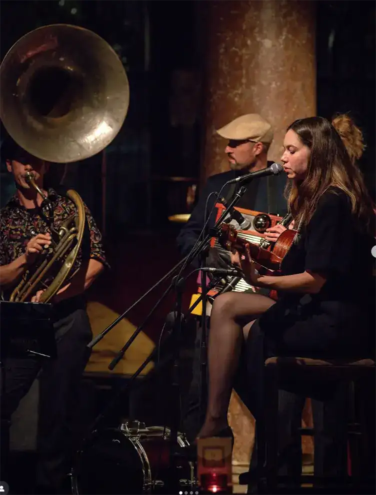 M&uacute;sicos tocando en un bar, mujer con guitarra y hombre con tuba.