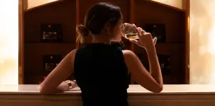 Persona de espaldas bebiendo vino en una bodega iluminada.